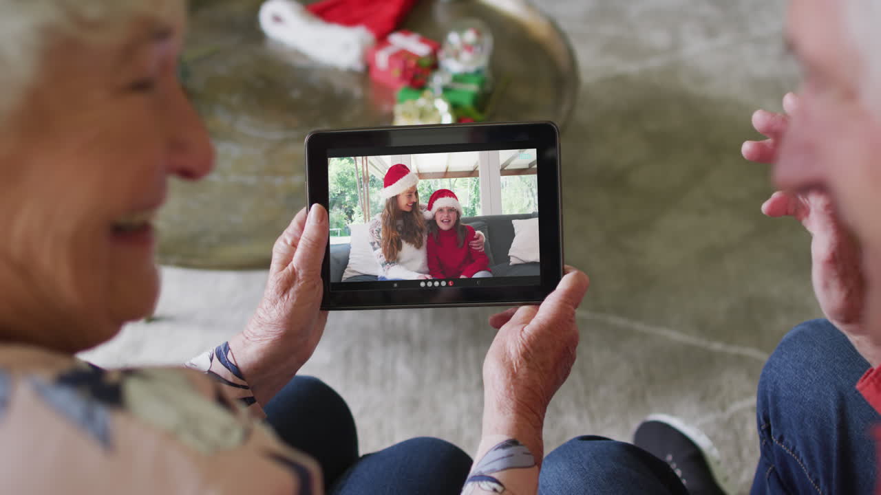 Coppia anziana caucasica che usa un tablet per una videochiamata di Natale con una famiglia felice sullo schermo