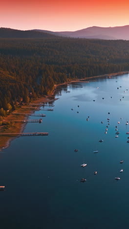 wooded shore of majestic lake tahoe at sunset. numerous boats sailing on the water. pink skies and mountains at backdrop. vertical video