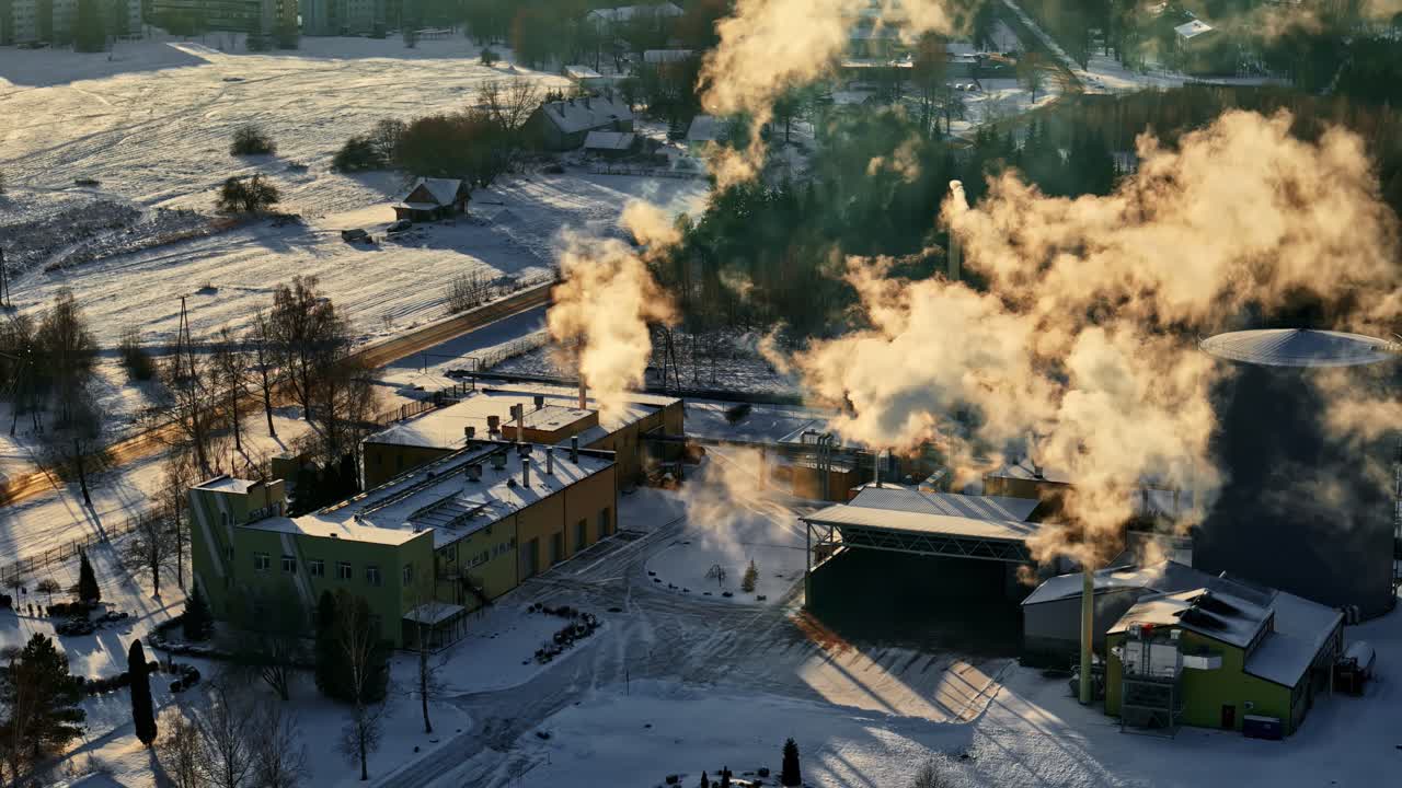Edifici di fabbrica coperti di neve che rilasciano dense nuvole di vapore su un complesso industriale in inverno.
