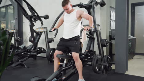 gym goer seated on weight machine balancing body and hands as he initiates chest press with controlled motion, engaged muscles, and focused effort under bright gym lighting and sleek equipment