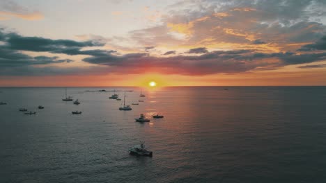 Rising-up,-revealing-a-beautiful,-golden-sun-setting,-anchored-boats-in-a-safe-harbor,-aerial