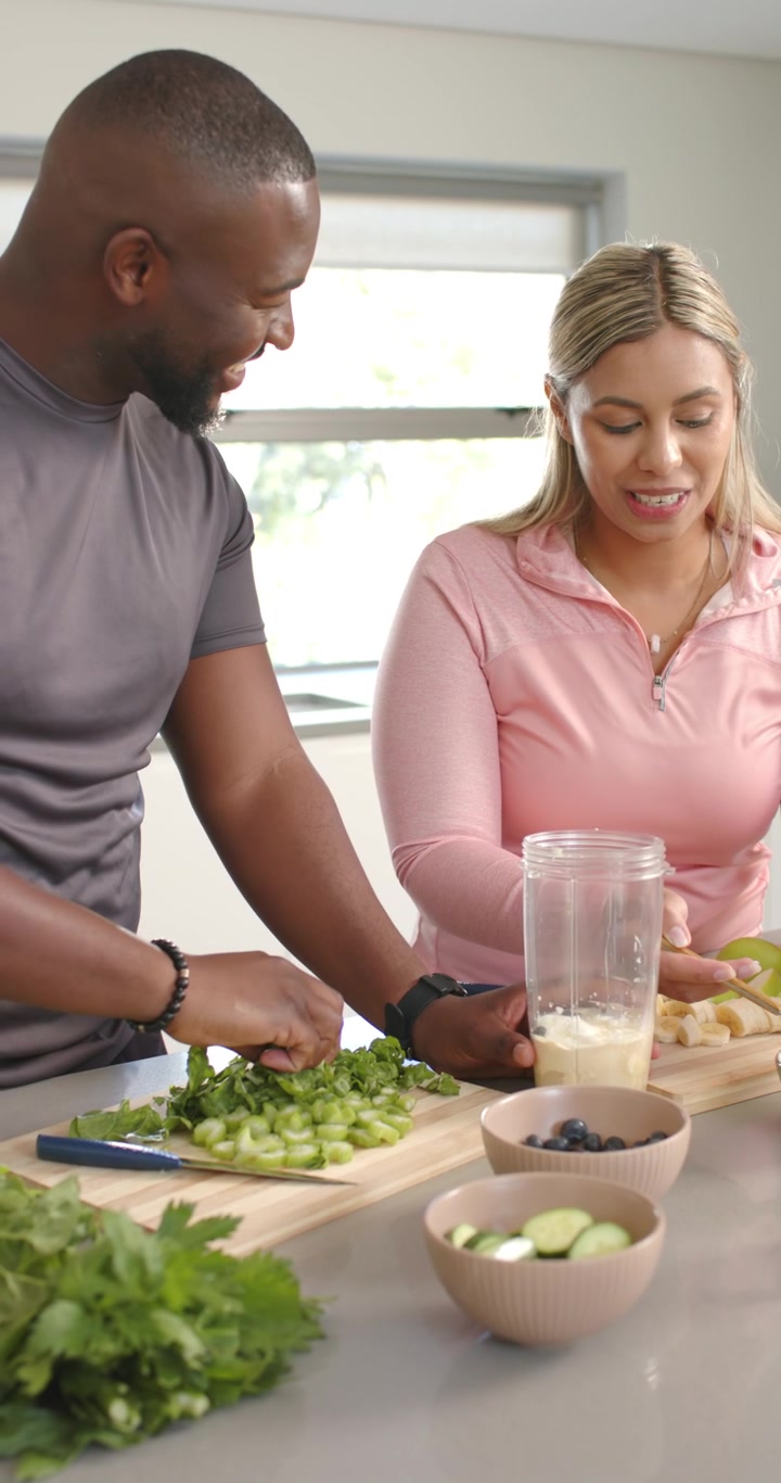 Vídeo vertical: Casal colocando iogurte no liquidificador, picando ervas, preparando smoothie na cozinha