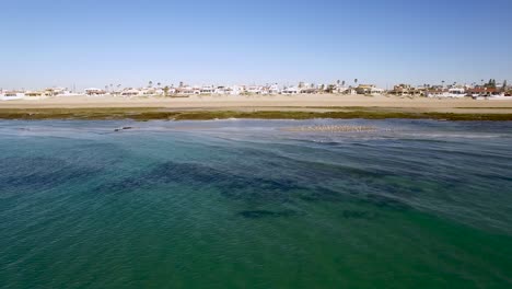 Aerial,-pan-low-angle-across-the-waves-and-shore-of-Rocky-Point,-Mexico-at-low-tide