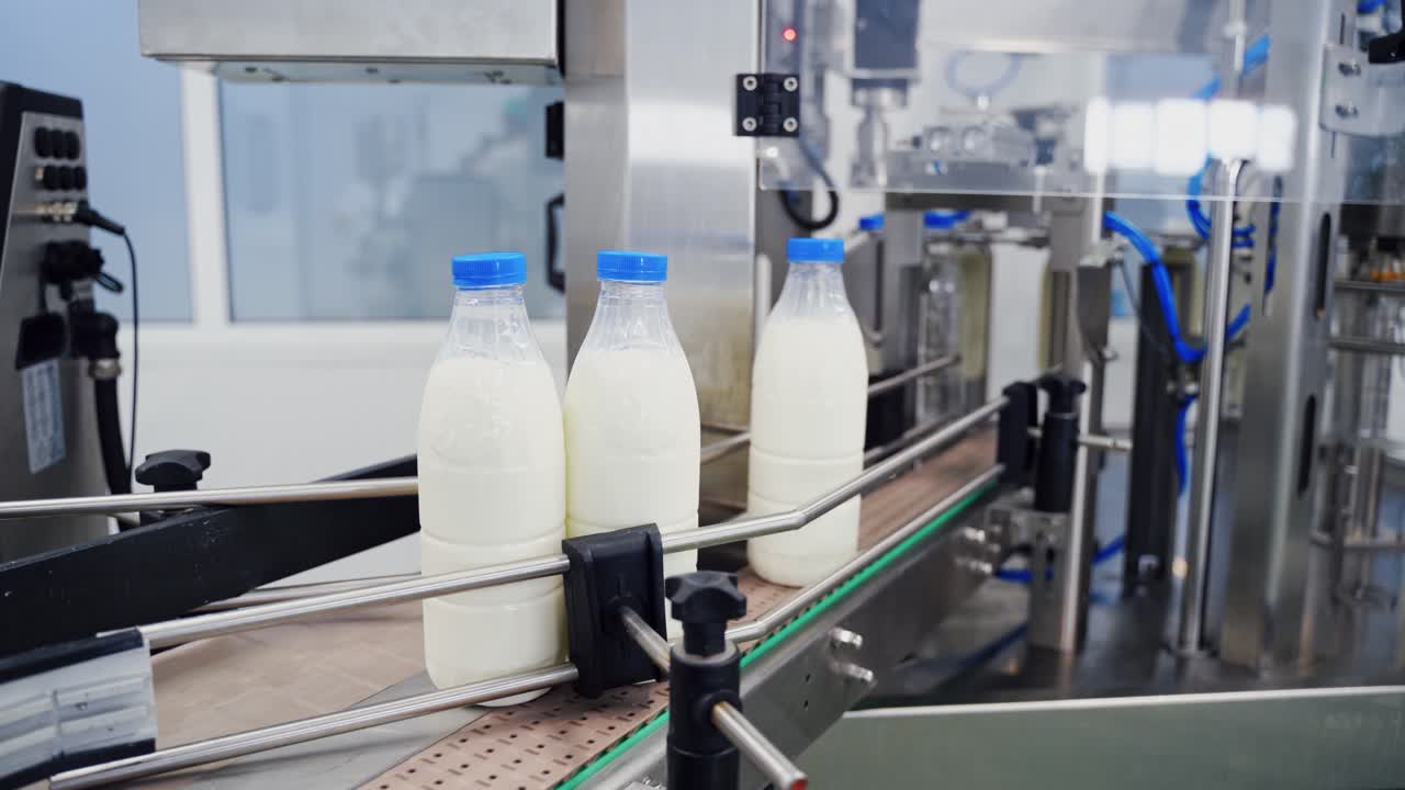 Milk bottles on conveyor belt. Hand is taking empty bottle from conveyor belt. Ready beverage production line at dairy factory. Close-up.