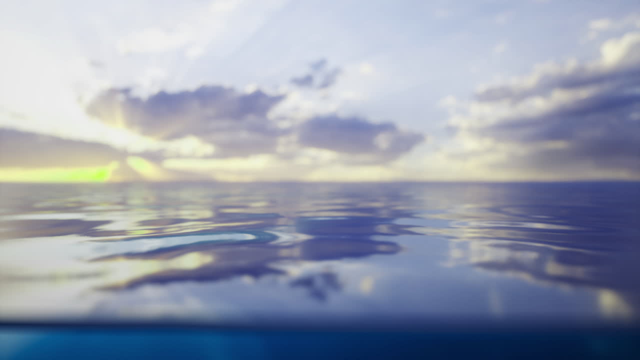 Calm ocean water reflects a vibrant sunset under soft clouds