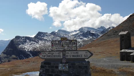 aerial drone flying low and near road sign of col de l'iseran with church and mountain range in background, france