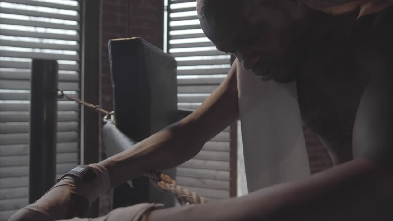 un boxeador negro sudoroso apoyándose en cuerdas entre rondas