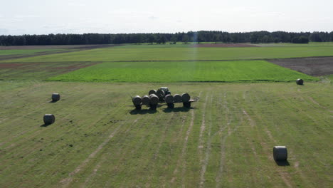 toma aérea de un tractor cargando dos grandes bolas de paja o fardos de heno en el carro con fardos de heno apilados