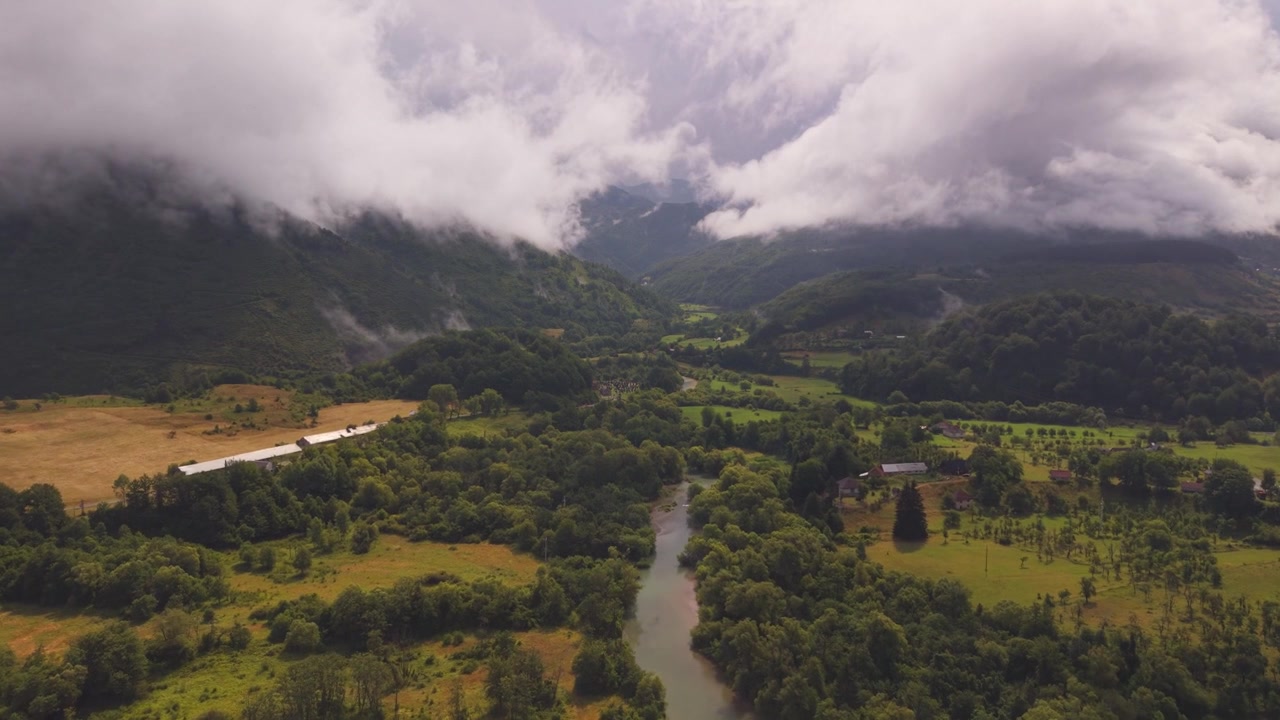 Veduta aerea del fiume Komaracka che scorre attraverso una valle verde lussureggiante con nebbia bassa e nuvole dense vicino a Plav, Montenegro
