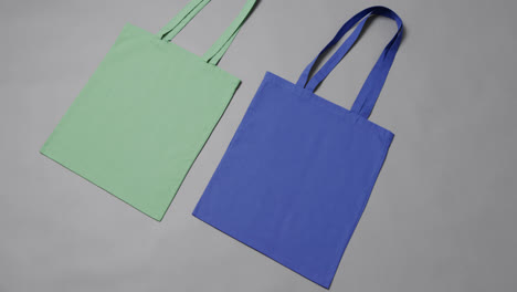 Close-up-of-green-and-blue-bags-on-grey-background,-with-copy-space,-slow-motion