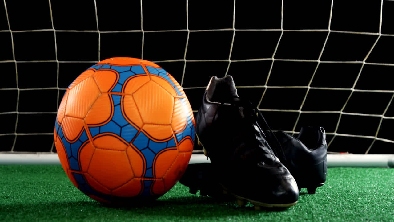 Primo piano di pallone da calcio e tacchetti su erba sintetica 4K