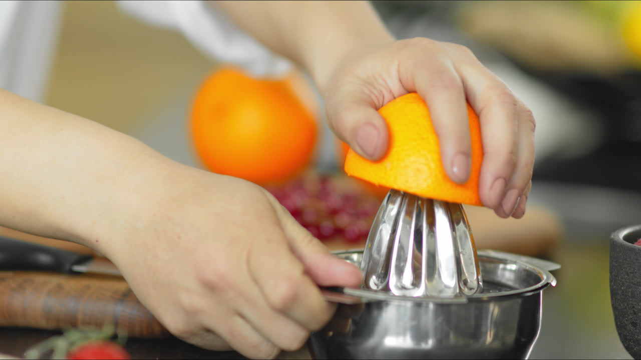Primer plano de una mujer joven cortando y exprimiendo una naranja.