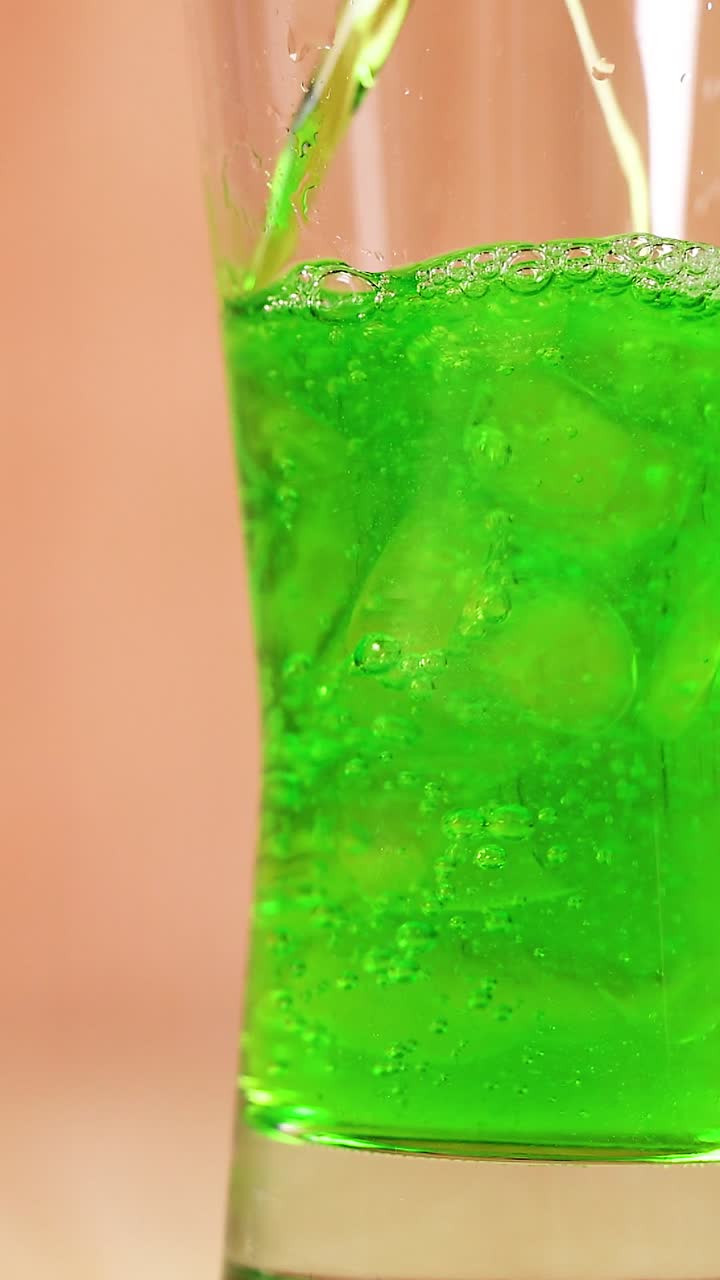 Uma bebida verde vibrante enche um copo alto com bolhas e efervescência