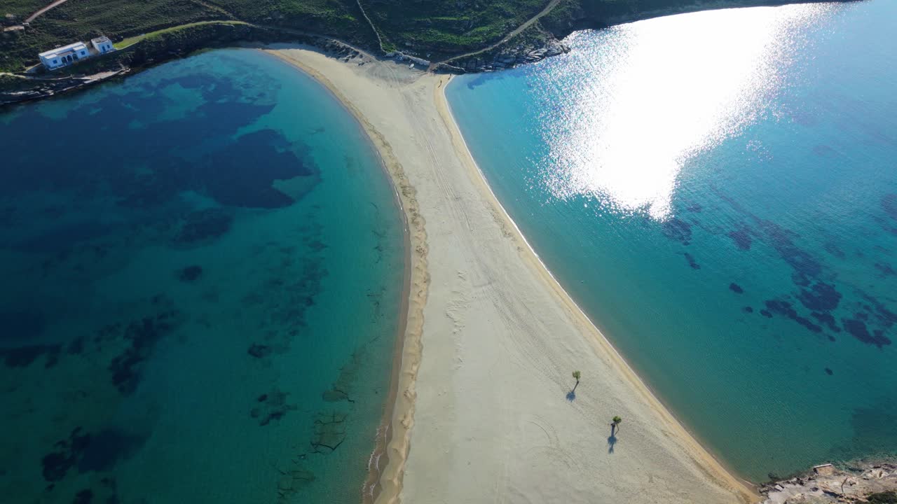 Aerial overview of Kolona Beach with sandbar splitting two bays, turquoise water and boats around the bend, panoramic orbit establishing