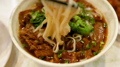 chopsticks lifting noodles from a savory bowl