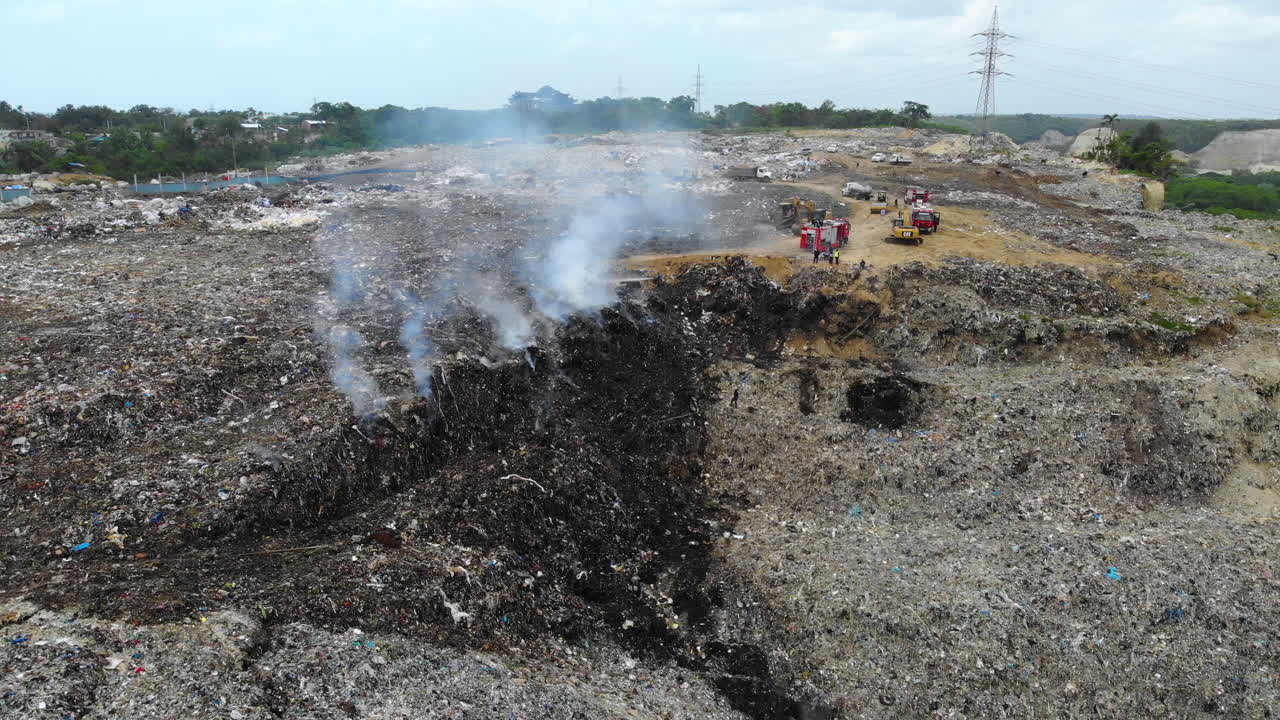 vista aérea alrededor de los bomberos, extinguiendo un incendio en un depósito de chatarra en medio de montones de basura, en evento, santo domingo, república dominicana - retroceso, disparo de drone
