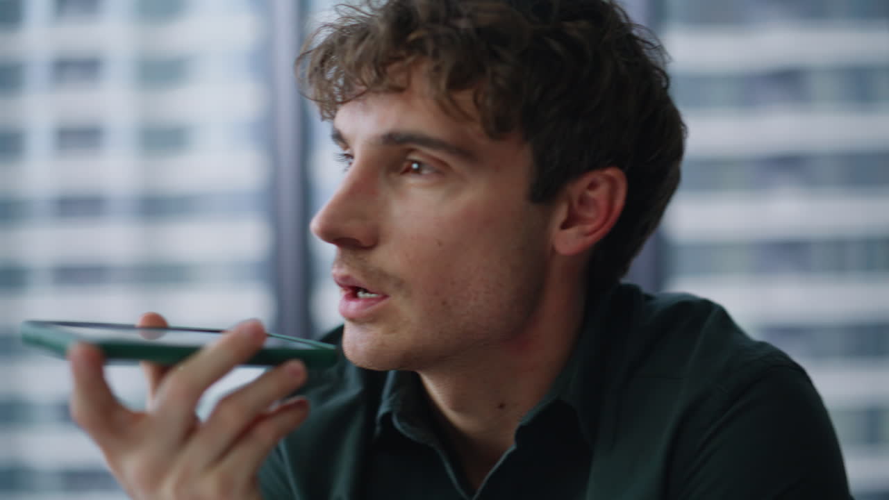 Closeup man recording voice message by cellphone sitting office. Serious manager