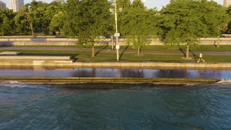 Aerial-tracking-shot-of-people-exercising-along-Chicago's-Lakeshore-Path-as-waves-crash-along-the-path-due-to-high-water-levels