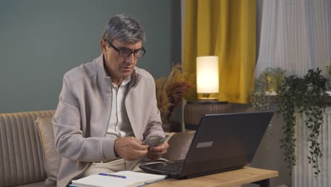 Old-man-looking-at-laptop-counting-money.