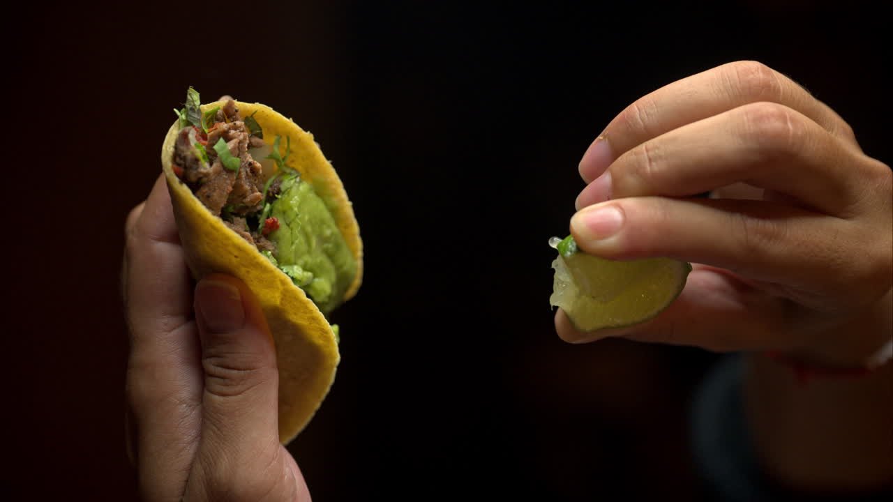 Lodret slowmotion af et par kvindehænder, der holder en traditionel mexicansk taco og presser lime over