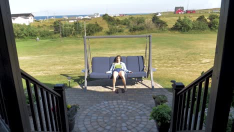 a young woman in shorts relaxes outside on a patio swing