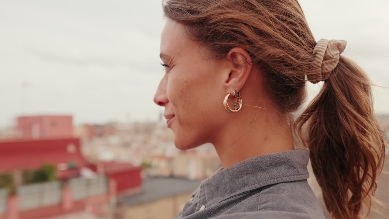 Primo piano di profilo di una giovane donna sorridente sul tetto di una città.
