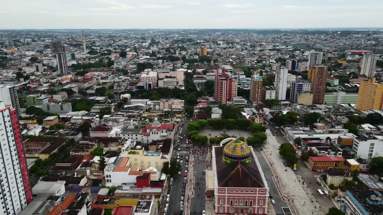 Teatro Amazonas y plaza principal en Manaos. Grandes multitudes se congregan en la calle durante una tarde nublada. Ascenso aéreo 4K con alejamiento sobre el teatro y la gran ciudad