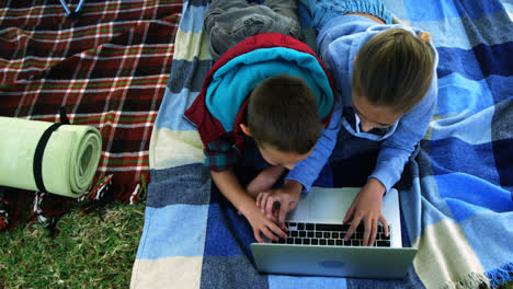 siblings using laptop outside the tent at campsite