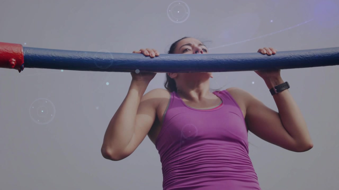 Video verticale: Donna in forma che esegue trazioni in palestra, afferrando una sbarra blu, con top viola e sovrapposizioni grafiche.