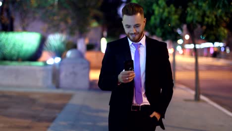 hombre de negocios caminando por la noche mirando el teléfono celular. guapo ejecutivo corporativo con teléfono inteligente por la noche