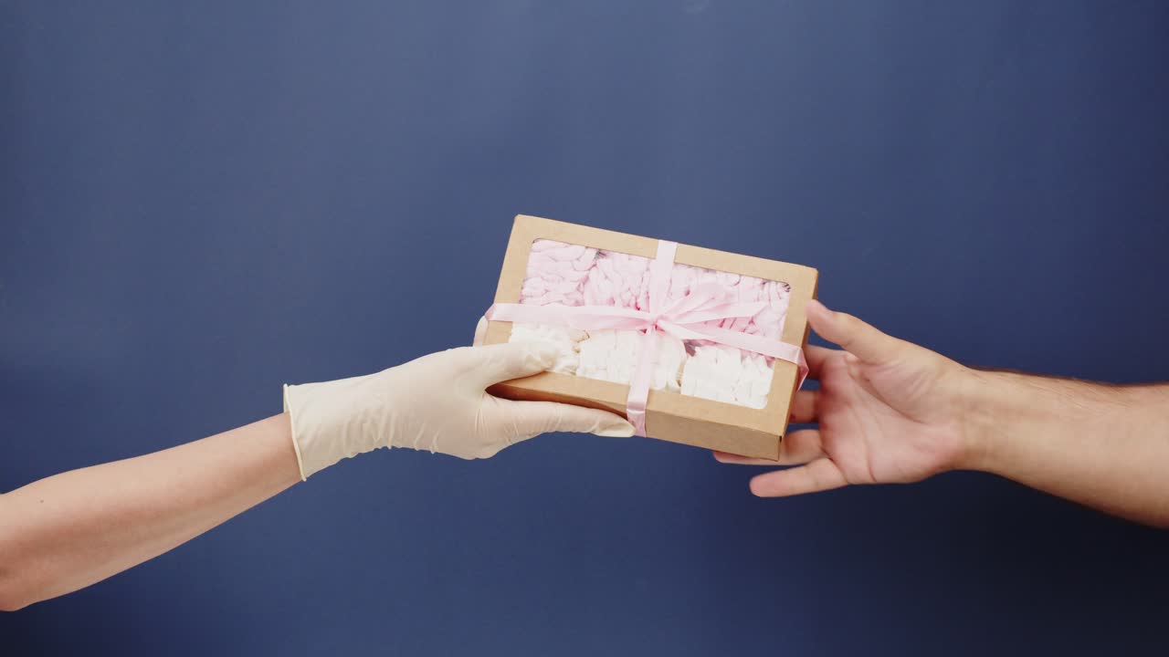 Mano guantata che consegna una scatola regalo di marshmallow a un'altra mano