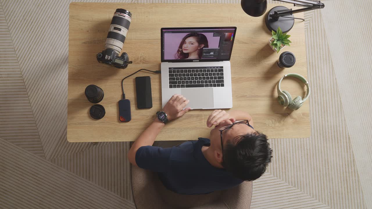 Top View Of Asian Male Editor Yawning And Sleeping While Sitting In The Workspace Using A Laptop Next To The Camera Editing Photo Of A Female At Home