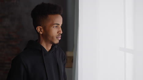 thoughtful black man in dark hoodie looks out of window