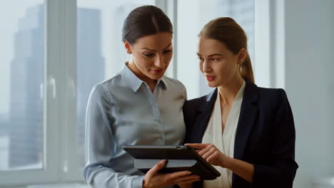 two businesswomen collaborating with a tablet in a modern office