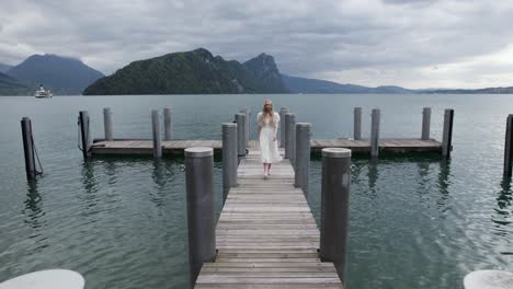 Junge-Frau-Im-Weißen-Kleid-Spaziert-Auf-Dem-Holzsteg-Im-Vierwaldstättersee,-Schweiz