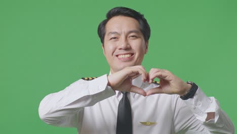 close up of asian male pilot making heart gesture and smiling on green screen background