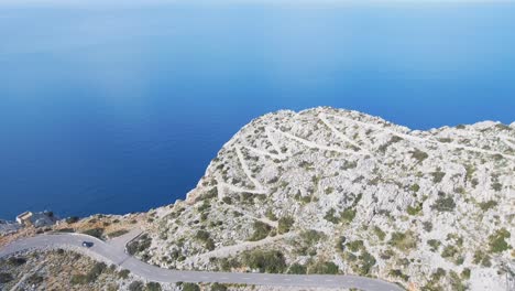 aerial footage in 4k of car driving on a curvy serpentine road with a stunning view of the mediterranean sea in mallorca, spain