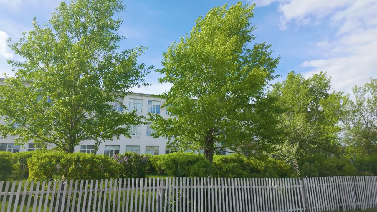 Old Building with Green Trees and a White Picket Fence Under a Blue Sky