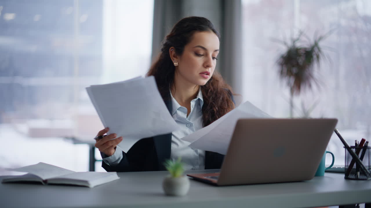 Confident businesswoman managing paperwork reviewing documents at laptop closeup