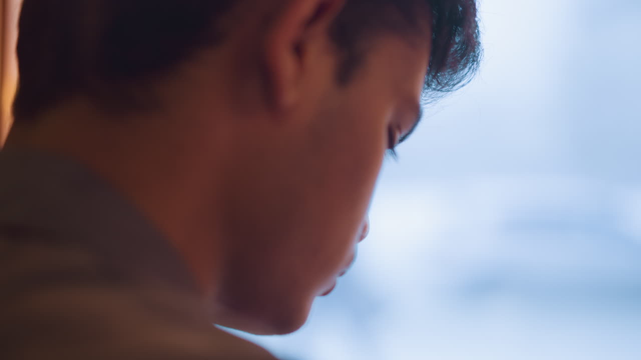 Close-up side view of young person deeply focused, head tilted downward in quiet contemplation or concentration, with soft lighting and blurred background suggesting introspective or creative mental activity