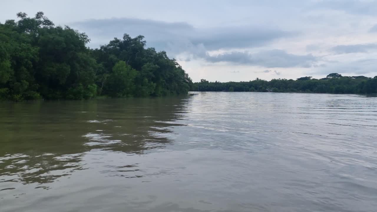 Foto di una barca sul fiume Pasur vicino a Mongla, Sundarbans, Bangladesh, con acque di marea, lussureggianti sponde tropicali e un cielo monsonico nuvoloso, che cattura il sereno ambiente del delta del fiume