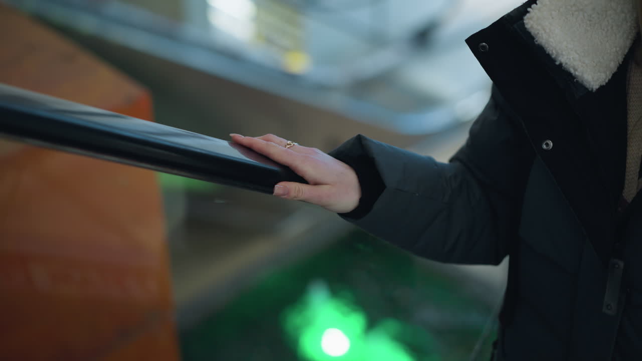 흐릿한 배경에서 반사되는 다채로운 박이는 불빛과 함께 움직이는 에스컬레이터의 레일에 배치 된 반지와 함께 손의 클로즈업, 쇼핑몰 환경에서 상승하는 에스칼레이터