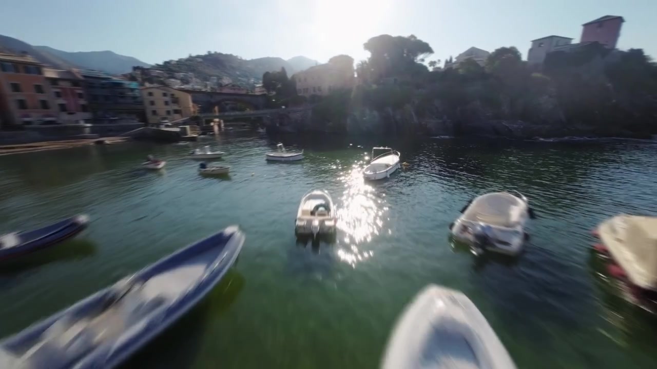 Drone FPV sorvola un piccolo porto con barche, edifici colorati e mare limpido