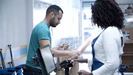 focused young man packing goods in paper bag and paying bill