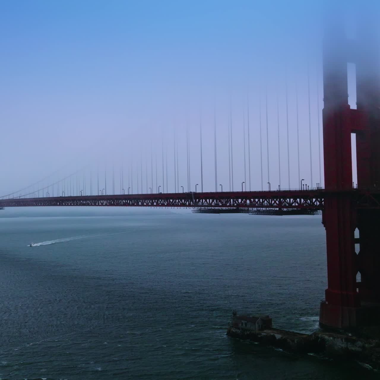 Well-known famous San Francisco landmark Golden Gate bridge. Upper parts of bridge are in fog. Boat sailing under the bridge
