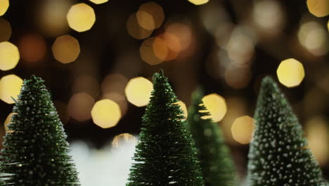 snow-dusted, spinning miniature christmas trees against golden bokeh lights with copy space