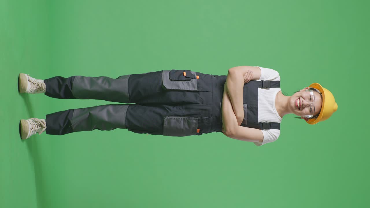Full Body Of Asian Woman Worker Wearing Goggles And Safety Helmet Smiling And Crossing Her Arms While Standing In The Green Screen Background Studio
