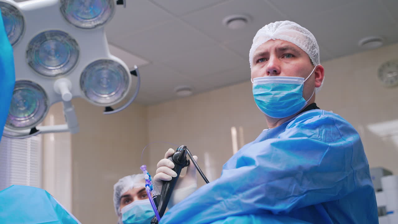 Portrait of a surgeon during operation. Serious male specialist in blue mask performing a surgery in the modern operating room in clinic.
