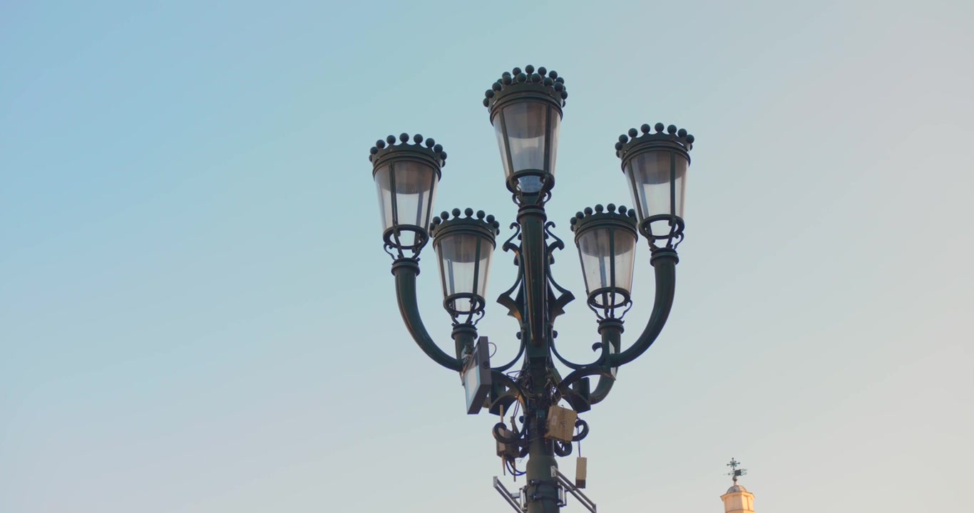 Farola ornamentada de múltiples cabezas se eleva hacia un cielo vespertino pálido en Turín, mostrada con una inclinación lenta hacia arriba
