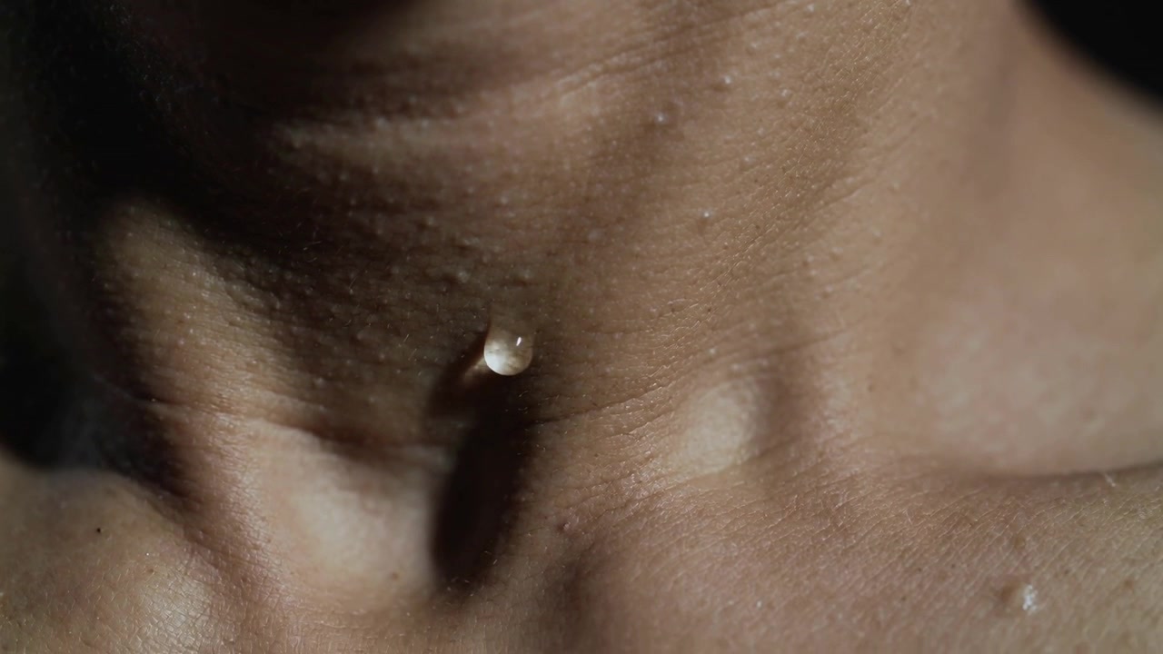 Gocciolina che scivola su collo o petto nudo in uno studio buio, la gravità che tira, la luce principale rivela i pori.